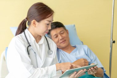 Asyalı kadın doktor hastane yatağı üzerinde oturan ve üst düzey hastayla - seçici odak noktası tartışıyor