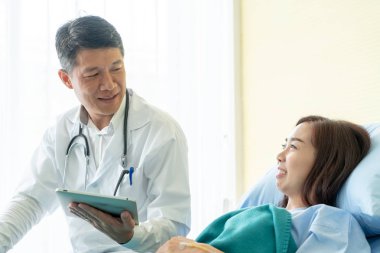 Asyalı kıdemli doktor hastane yatağında oturup kadın hastalarla konuşuyor. Seçici odak noktası.