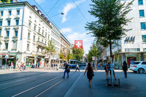 ZURICH, SWITZERLAND - AUG 23, 2018: A tram drives down the center of Bahnhofstrasse while people walk on the sidewalks in Zurich City, Switzerland.