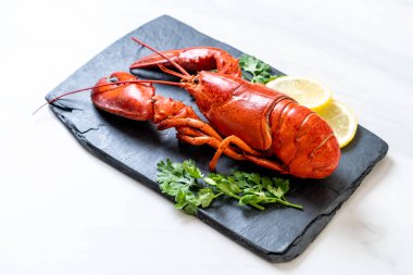 Sebzeli kırmızı ıstakoz ve siyah tabakta limon.