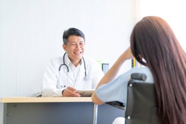 Asyalı doktor ve hasta bir şey masada otururken görüşüyorlar