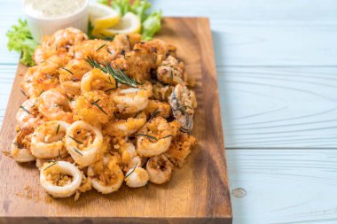 Tahta üzerinde sos olan kızarmış deniz ürünleri (mürekkep balıkları, karidesler, midyeler)