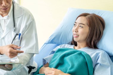 Asyalı kıdemli doktor hastane yatağında oturup kadın hastalarla konuşuyor. Seçici odak noktası.