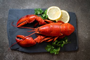 Sebzeli kırmızı ıstakoz ve siyah tabakta limon.