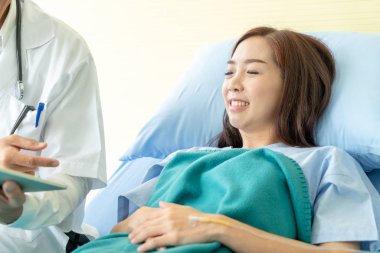 Asyalı kıdemli doktor hastane yatağında oturup kadın hastalarla konuşuyor. Seçici odak noktası.