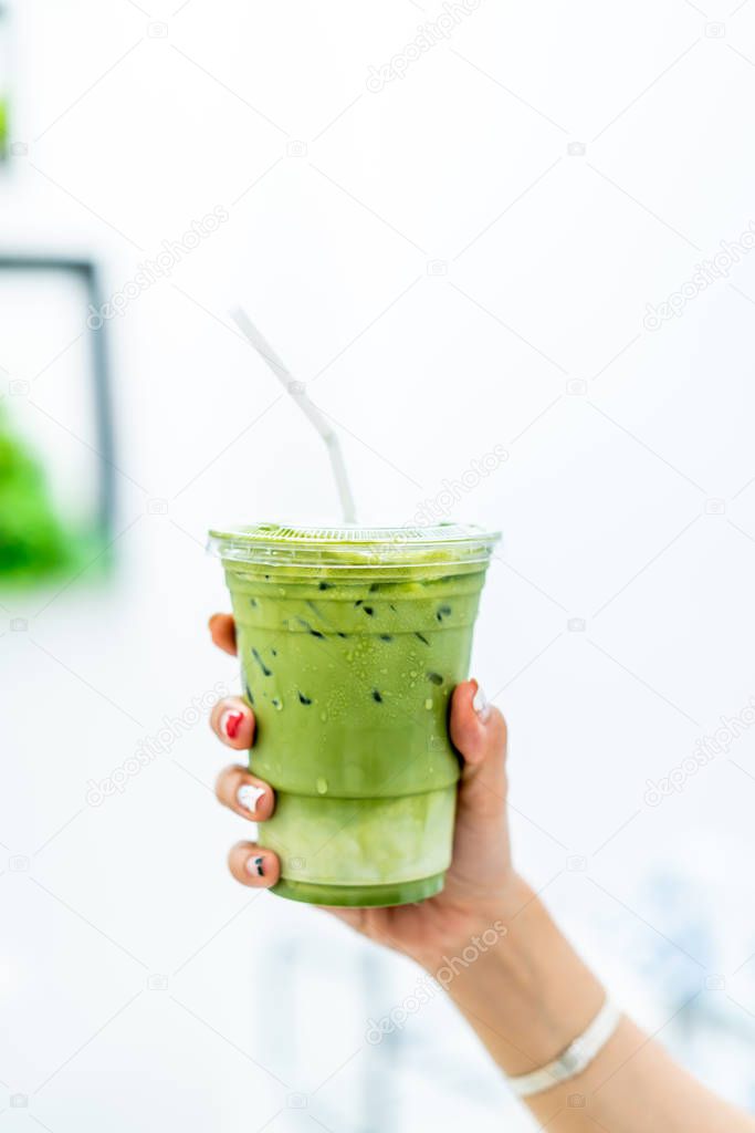 close-up hand holding iced matcha latte green tea cup