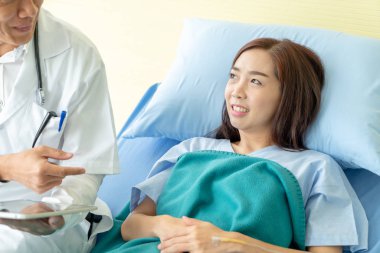 Asyalı kıdemli doktor hastane yatağında oturup kadın hastalarla konuşuyor. Seçici odak noktası.