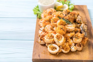 Tahta üzerinde sos olan kızarmış deniz ürünleri (mürekkep balıkları, karidesler, midyeler)