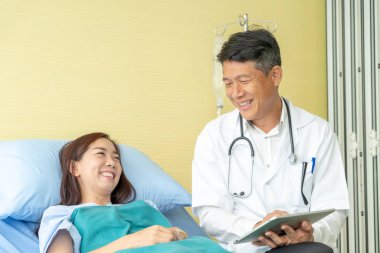 Asyalı kıdemli doktor hastane yatağında oturup kadın hastalarla konuşuyor. Seçici odak noktası.