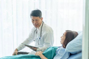 Asyalı kıdemli doktor hastane yatağında oturup kadın hastalarla konuşuyor. Seçici odak noktası.