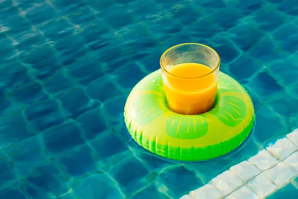 Copo de sumo de laranja com anel de natação na piscina exterior — Fotografia de Stock