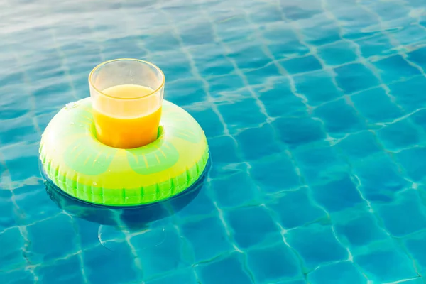 Orange juice glass with swim ring at outdoor swimming pool — Stock Photo, Image