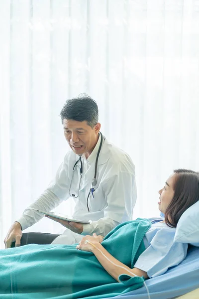 Asijské starší lékař sedí na nemocniční posteli a diskutovat s — Stock fotografie