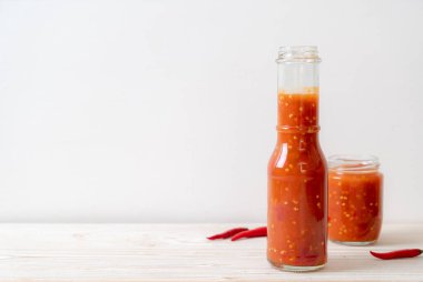 Şişede kırmızı biber ya da kırmızı biber sosu ve arka planda kavanoz.