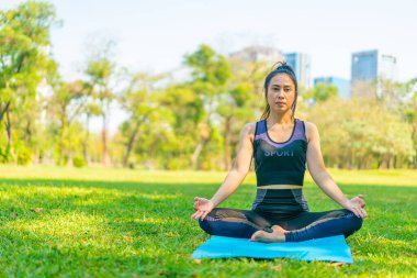 Asyalı kadın yoga yapıyor ve yazın yeşil parkta spor kıyafetleriyle rahatlıyor.