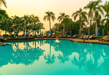 Gün batımında yüzme havuzunda şemsiyeli plaj sandalyesi ya da bilardo yatağı