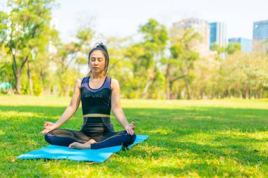 Asyalı kadın yoga yapıyor ve yazın yeşil parkta spor kıyafetleriyle rahatlıyor.