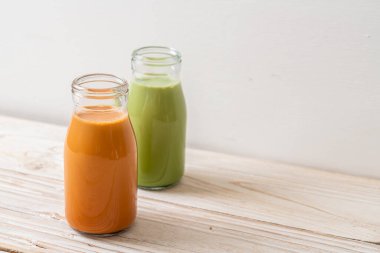 Thai sütlü çay ve ahşap masada şişe içinde yeşil çay.