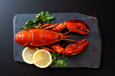 Sebzeli kırmızı ıstakoz ve siyah tabakta limon.