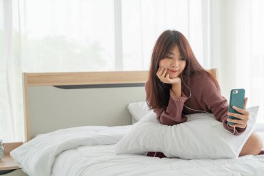 Güzel Asyalı kadınlar yatakta akıllı telefon oynuyorlar.