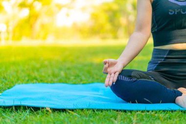Asyalı kadın yoga yapıyor ve yazın yeşil parkta spor kıyafetleriyle rahatlıyor.