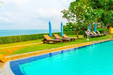 Sandalye havuzu ve şemsiyeyle okyanus arka planında yüzme havuzu