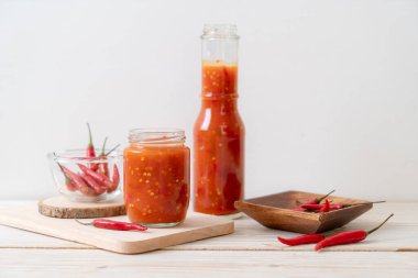 Şişede kırmızı biber ya da kırmızı biber sosu ve arka planda kavanoz.