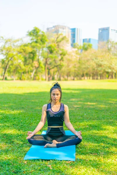 Asyalı kadın yoga yapıyor ve yazın yeşil parkta spor kıyafetleriyle rahatlıyor.
