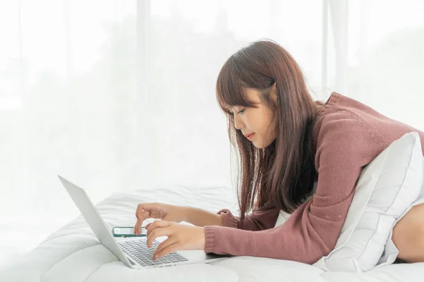 Asian women working with laptop on bed at home