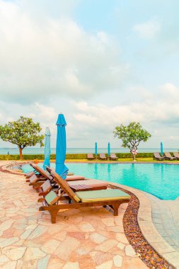 Sandalye havuzu ve şemsiyeyle okyanus arka planında yüzme havuzu