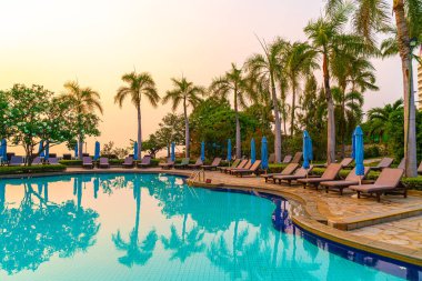 Gün batımında yüzme havuzunda şemsiyeli plaj sandalyesi ya da bilardo yatağı