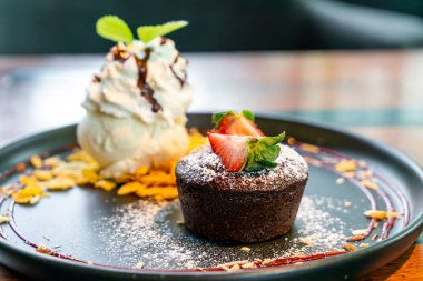 Çilekli çikolatalı lav ve siyah tabakta vanilyalı dondurma.