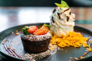 Çilekli çikolatalı lav ve siyah tabakta vanilyalı dondurma.