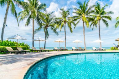 Güzel tropikal plaj ve deniz şemsiyesi ve sandalyesi otel tatil ve tatil için yüzme havuzunda.