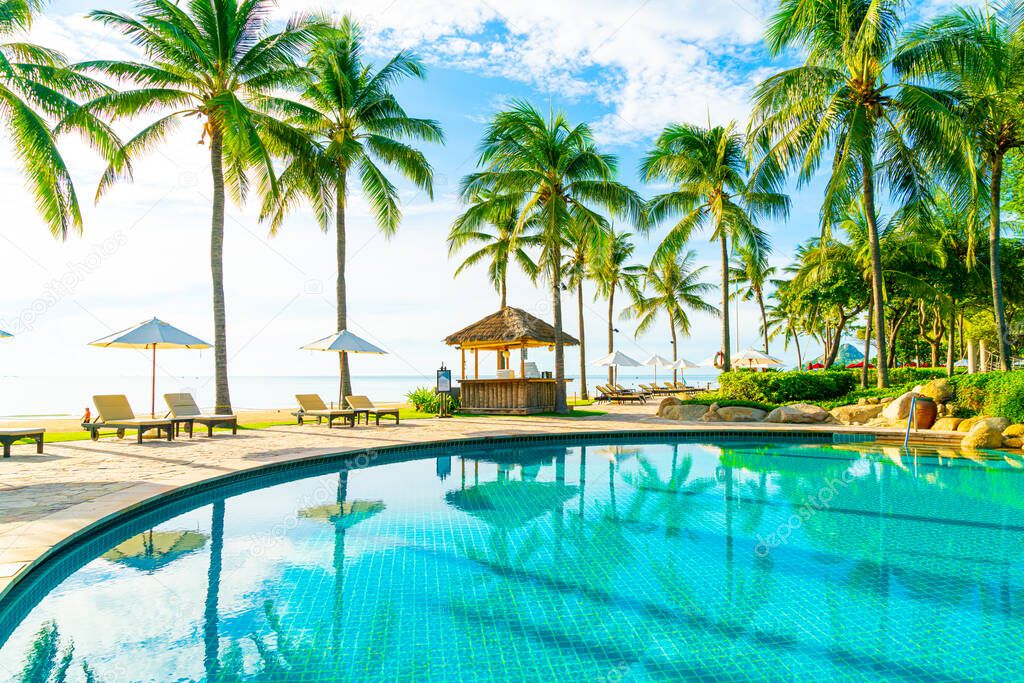 Beautiful luxury umbrella and chair around outdoor swimming pool in hotel and resort with coconut palm tree on blue sky - vacation and holiday concept