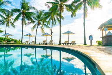 Otelde açık havuzda güzel bir şemsiye ve sandalye ve gün batımında hindistan cevizi palmiyesi ağacı olan bir tatil ve tatil konsepti.