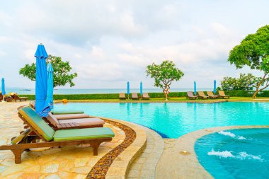 Sandalye havuzu ve şemsiyeyle okyanus arka planında yüzme havuzu