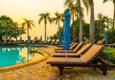 Gün batımında yüzme havuzunda şemsiyeli plaj sandalyesi ya da bilardo yatağı