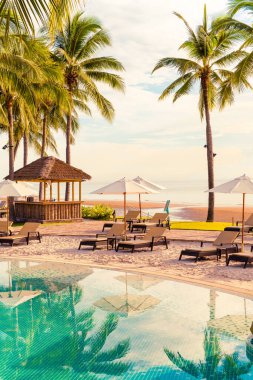 Otelde açık havuzda güzel bir şemsiye ve sandalye ve gün batımında hindistan cevizi palmiyesi ağacı olan bir tatil ve tatil konsepti.