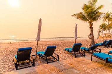 Güneş doğarken palmiye ağacı ve deniz plajı olan şemsiye koltuğu plajı - tatil ve tatil konsepti