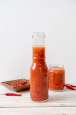 Şişede kırmızı biber ya da kırmızı biber sosu ve arka planda kavanoz.