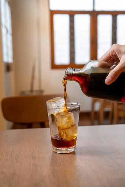 pouring cold brew coffee in glass with ice cube on wood table