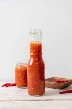 Şişede kırmızı biber ya da kırmızı biber sosu ve arka planda kavanoz.