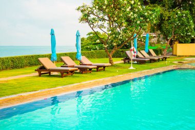 Sandalye havuzu ve şemsiyeyle okyanus arka planında yüzme havuzu