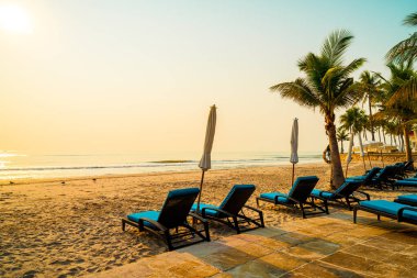 Güneş doğarken palmiye ağacı ve deniz plajı olan şemsiye koltuğu plajı - tatil ve tatil konsepti