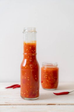 Şişede kırmızı biber ya da kırmızı biber sosu ve arka planda kavanoz.