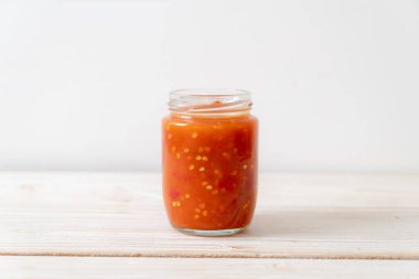 Şişede kırmızı biber ya da kırmızı biber sosu ve arka planda kavanoz.