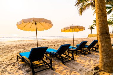 Güneş doğarken palmiye ağacı ve deniz plajı olan şemsiye koltuğu plajı - tatil ve tatil konsepti
