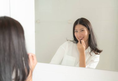 Genç ve güzel Asyalı kadın aynaya bakıyor.