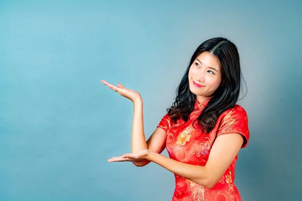beautiful young asian woman wear red chinese traditional dress with hand presenting on side in blue background
